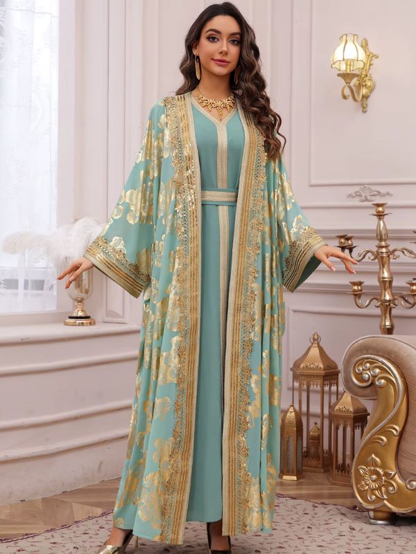 Femme en caftan turquoise à fleurs dorées, bras écartés, dans un intérieur élégant aux accents dorés