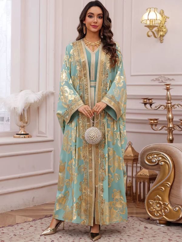 Femme portant un caftan marocain turquoise à motifs floraux dorés sur une robe assortie, dans un décor raffiné