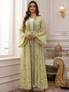 Une femme en caftan marocain fleuri vert pâle pose près d’une fenêtre orientale