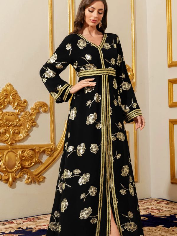Caftan noir imprimé floral doré, main posée sur la ceinture brodée, regard baissé
