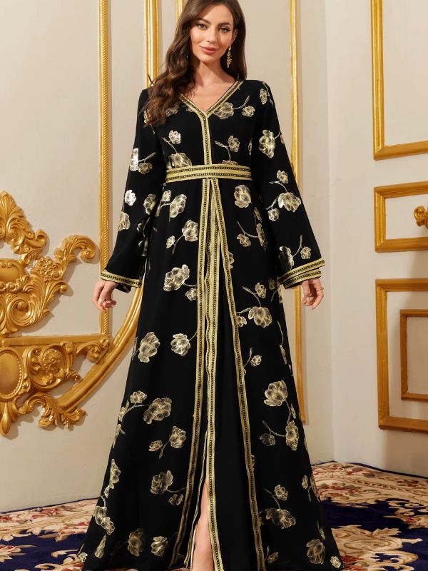 Caftan noir à fleurs dorées et bordure chaînée, debout face à un tapis à motifs bleus