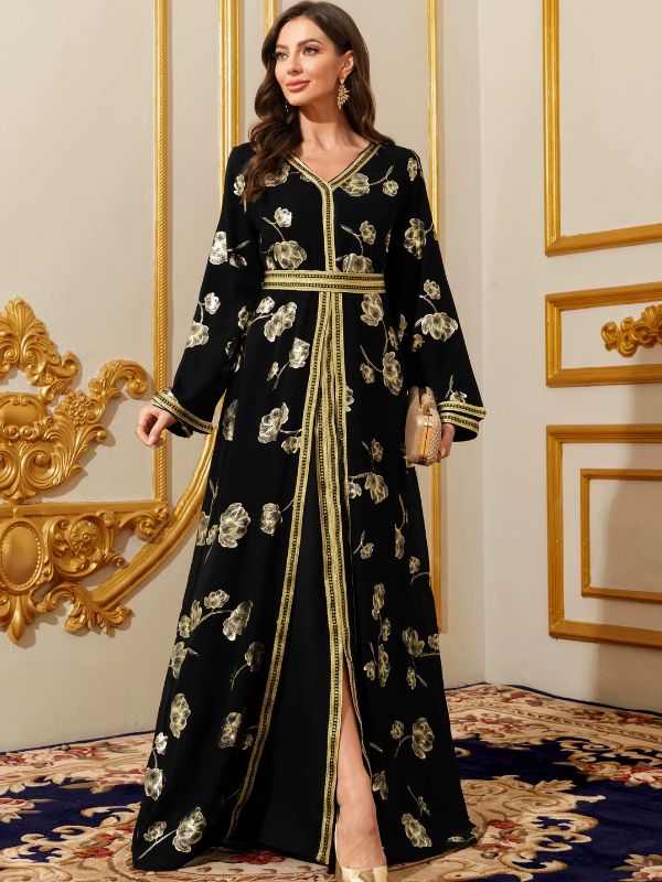Caftan noir fleuri à galon doré et pochette assortie, porté devant un panneau mural doré