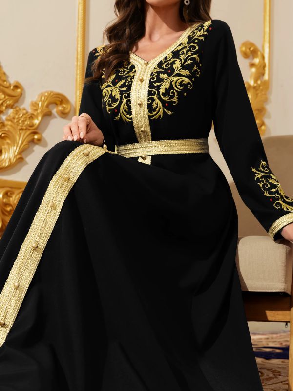 Vue rapprochée d'un caftan noir en position assise, broderies florales dorées au buste et galon or.