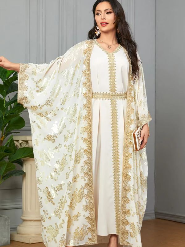 Une femme pose en caftan blanc fluide à broderies dorées