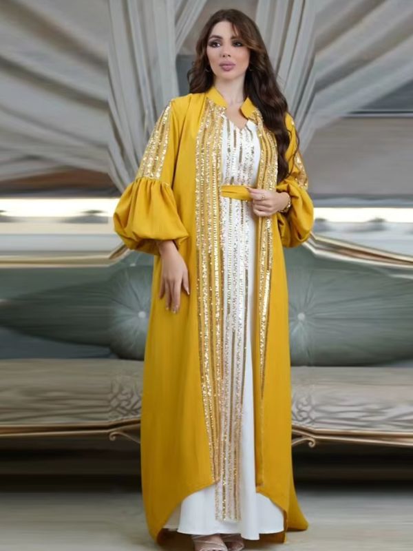 Femme portant un caftan jaune à manches ballon et sequins dorés sur une robe longue blanche, dans un décor élégant.