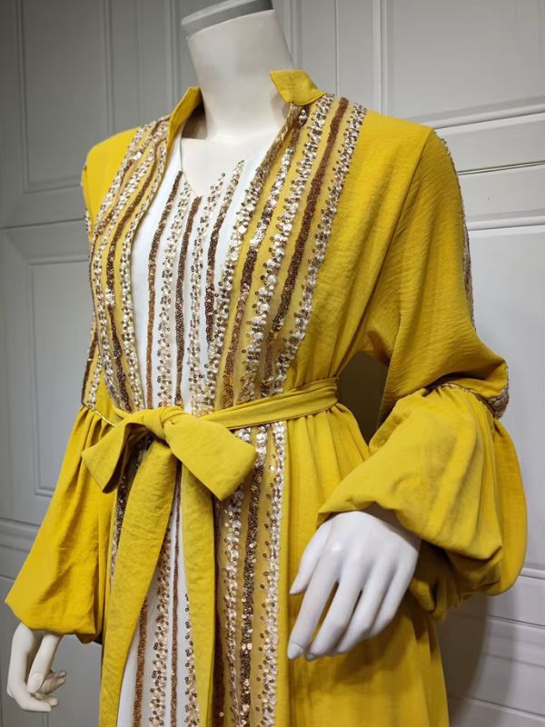 Vue de trois quarts d'un caftan jaune à manches bouffantes, orné de rangées de sequins dorés et blancs.