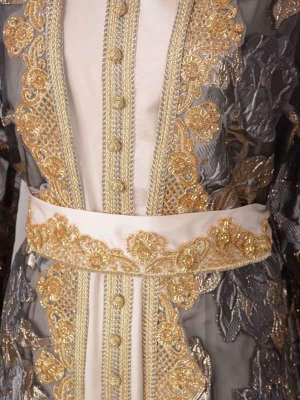 Détail des galons dorés, des perles et des boutons de la robe crème sous le manteau gris ardoise