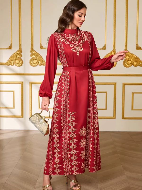 Caftan marocain mariage rouge porté de face avec une pochette perlée, frises dorées verticales sur la jupe