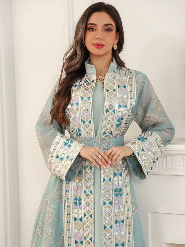 Vue rapprochée d'une femme en caftan turquoise à col montant, orné de broderies géométriques multicolores.