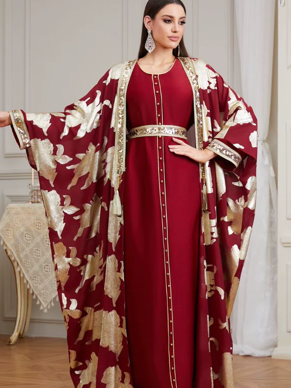 Femme portant un caftan marocain bordeaux avec cape à motifs dorés et ceinture ornée, vue de trois quarts