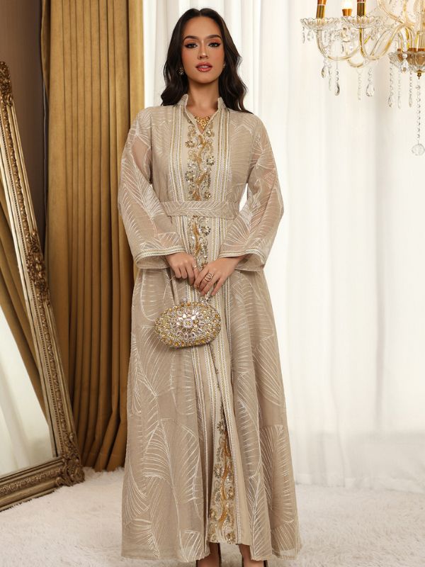 Femme en caftan ivoire à motifs de feuilles brodées et broderies dorées, devant un lustre en cristal.