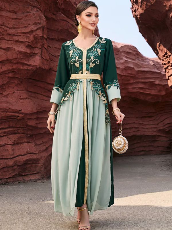 Femme portant un caftan marocain bicolore vert forêt et vert d'eau à broderies florales dorées, debout de face devant des rochers rouges