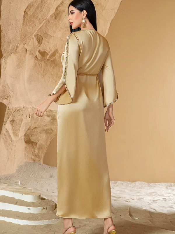 Caftan doré en satin brillant, manches à revers perlé, vue de dos devant un décor désertique