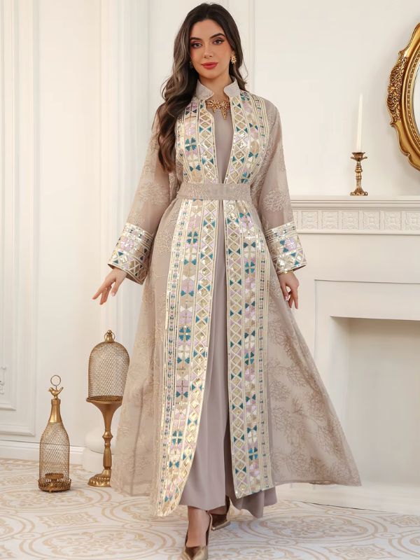Femme en caftan marocain champagne brodé, mains écartées, dans un intérieur raffiné aux tons clairs.