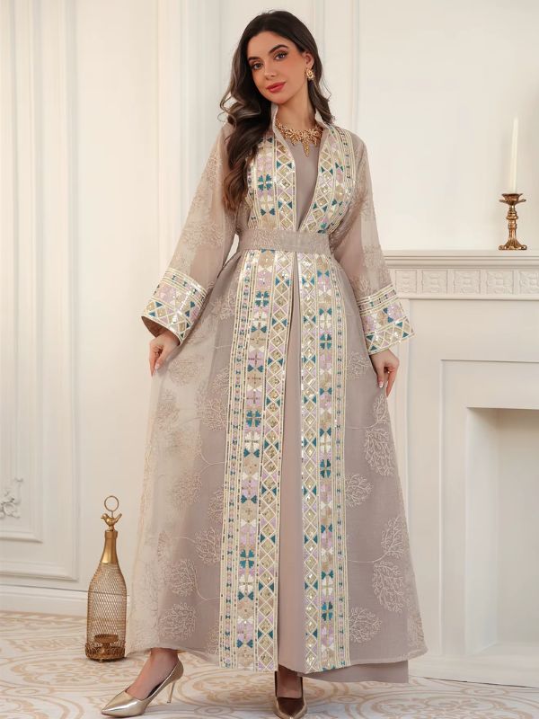Femme en caftan champagne en tulle brodé, porté ouvert sur une robe assortie, devant une cheminée blanche.
