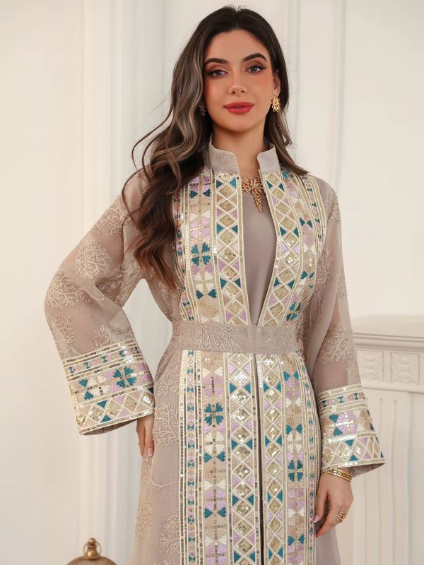 Femme portant un caftan champagne brodé de motifs géométriques multicolores, ceinturé à la taille.