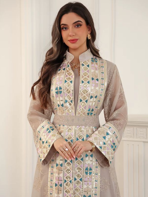 Femme en caftan champagne en tulle brodé, porté ouvert sur une robe assortie, devant une cheminée blanche.