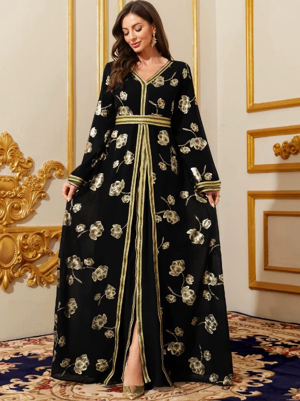 Femme portant un caftan marocain noir fleuri d'or, manches amples et ceinture galonnée, posant dans un décor luxueux