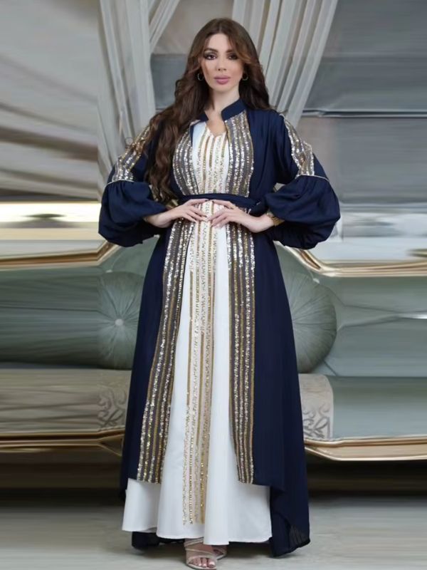 Femme portant un caftan bleu royal à sequins dorés sur une robe longue blanche, dans un décor élégant.