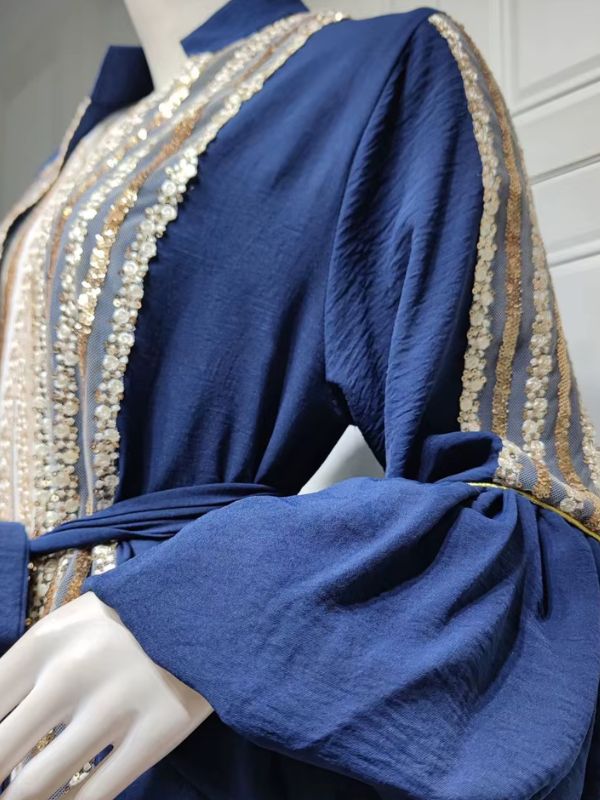 Gros plan sur les détails d'un caftan bleu royal : broderies de sequins dorés et manche bouffante.