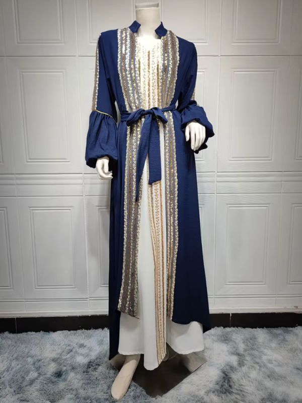 Femme portant un caftan bleu royal à sequins dorés sur une robe longue blanche, dans un décor élégant.