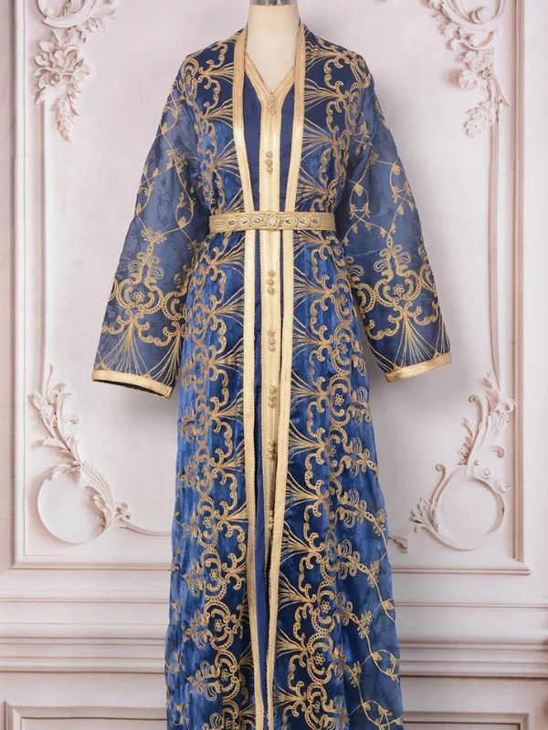 Mannequin portant un caftan marocain bleu nuit orné de broderies argentées, debout dans un décor élégant
