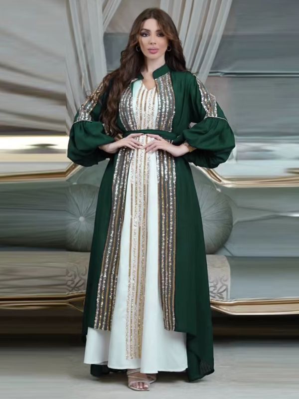 Femme portant un caftan vert émeraude à sequins dorés sur une robe longue blanche, dans un décor élégant.