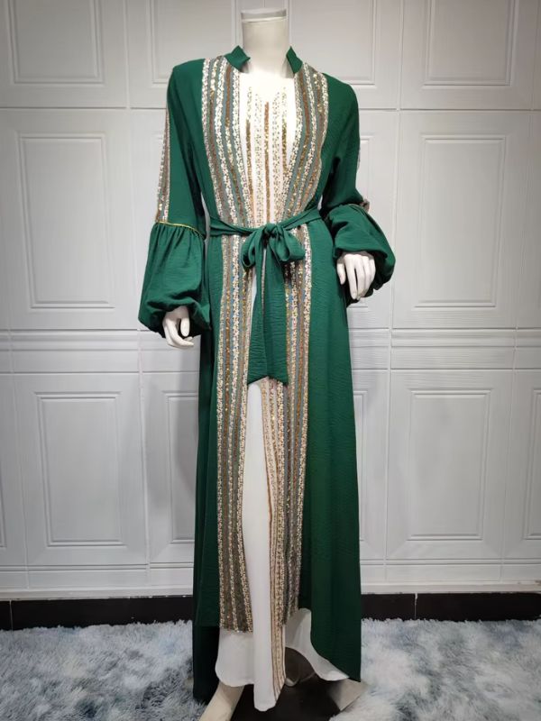 Caftan marocain vert émeraude en pied sur mannequin, porté ouvert sur une robe blanche, orné de sequins dorés.