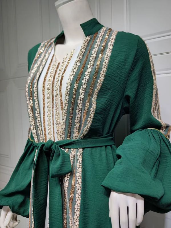Femme portant un caftan vert émeraude à sequins dorés sur une robe longue blanche, dans un décor élégant.