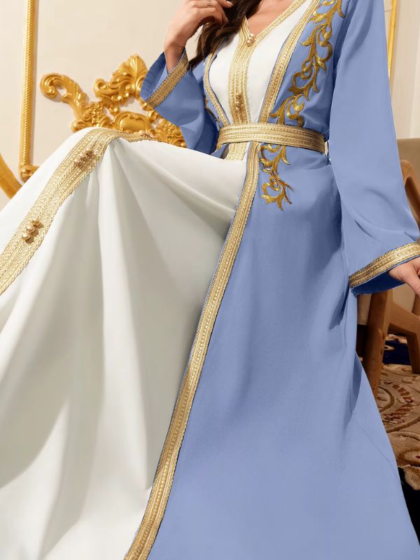 Gros plan sur un caftan azur et blanc aux broderies dorées, ceinturé de galon doré scintillant
