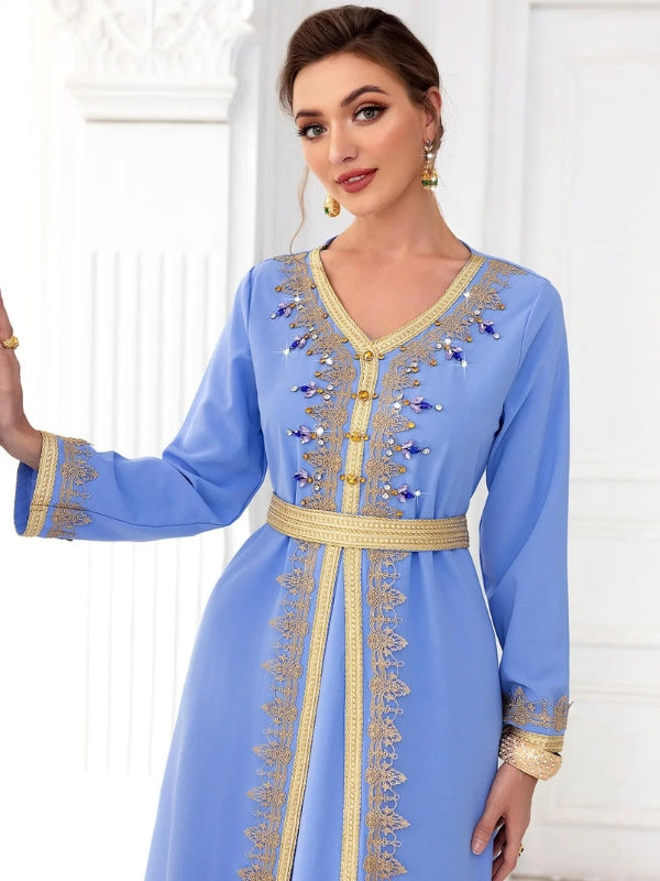 La femme porte un caftan bleu ciel orné de broderies dorées qui mettent en valeur le col en V, les manches, et descendent le long de l'ouverture frontale. Ces détails dorés ajoutent une touche d'élégance à sa tenue. La ceinture assortie à la taille accentue sa silhouette, tandis qu'elle accessoirise son look avec des sandales à talons et une pochette dorée. Sa coiffure relevée met en avant ses boucles d'oreilles pendantes, complétant ainsi un ensemble chic et sophistiqué, parfait pour des occasions formelle