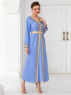 La femme porte un caftan bleu ciel avec des broderies dorées sur le devant, les manches, et autour du col en V. La robe est cintrée à la taille par une ceinture assortie qui accentue sa silhouette. Elle complète son look avec des boucles d&#39;oreilles pendantes et des talons dorés, tout en tenant une pochette dorée. Sa coiffure relevée et élégante met en valeur son visage, et l&#39;ensemble de sa tenue respire la sophistication et l&#39;élégance, idéal pour des événements formels ou des occasions spéciales