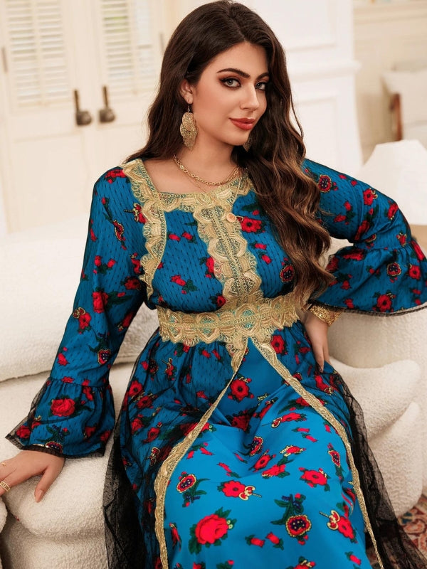 La femme sur cette image porte un magnifique caftan bleu avec des motifs floraux rouges et des détails dorés. Le caftan est orné de broderies dorées qui ajoutent une touche élégante à la tenue. Les manches sont légèrement évasées, ce qui donne une allure fluide et gracieuse. La femme a de longs cheveux ondulés qui tombent sur son épaule droite