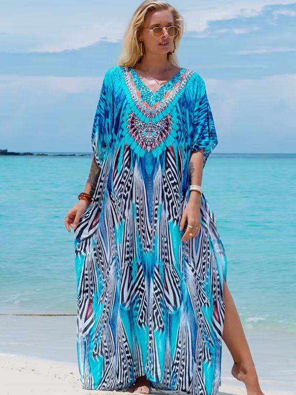 Une femme vêtue d’une djellaba turquoise imprimée aux inspirations orientales, marchant sur le sable face à la mer