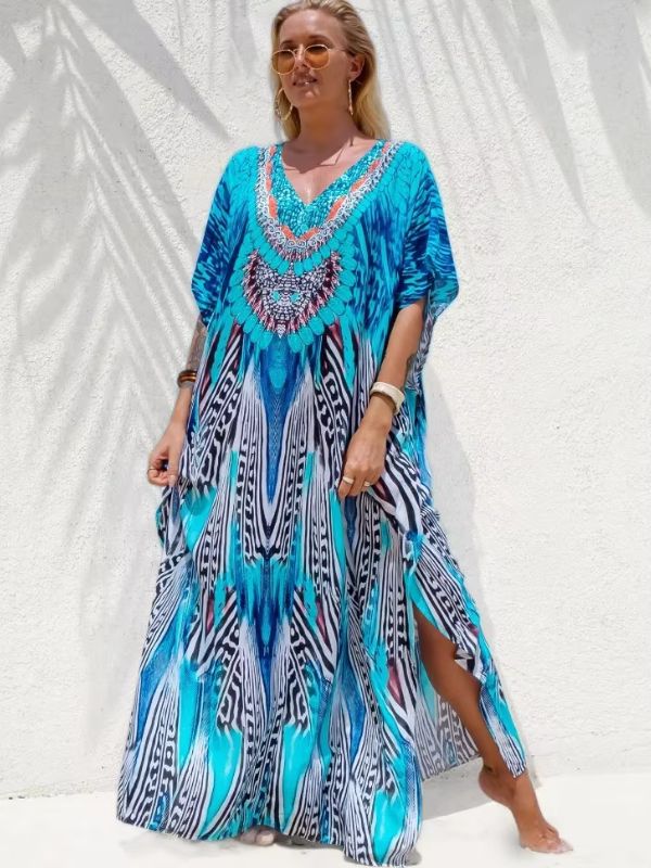 Une femme présente une djellaba ample aux tons turquoise et noir, fendue sur le côté, posant contre un mur blanc