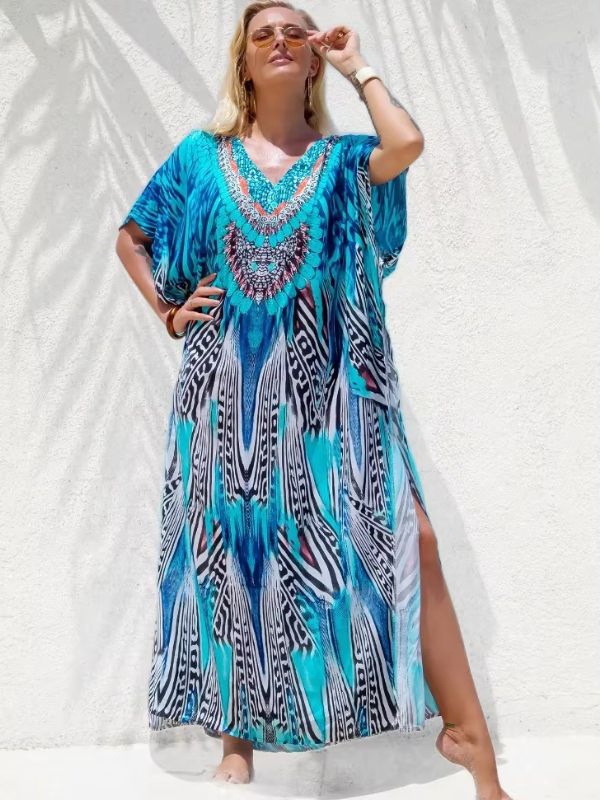 Une femme présente une djellaba ample aux tons turquoise et noir, fendue sur le côté, posant contre un mur blanc