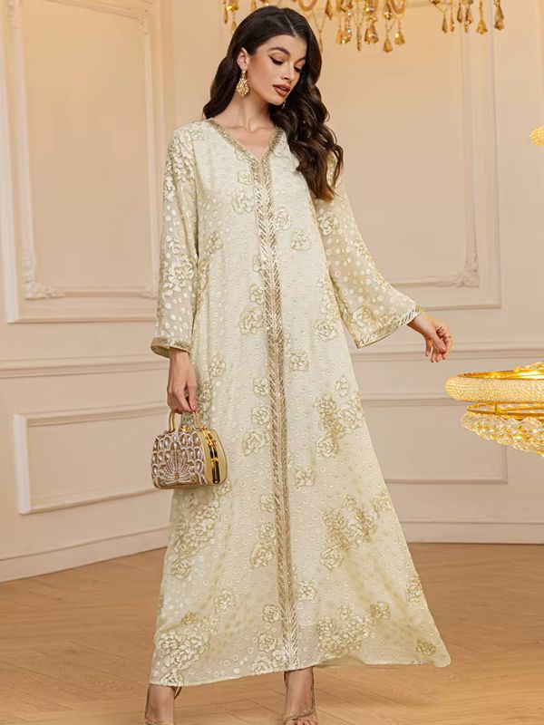 Femme tenant un sac doré en djellaba claire décorée de fleurs brodées