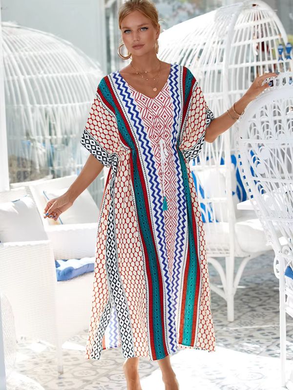 Une femme porte une djellaba multicolore d’inspiration andalouse, posant dans un salon lumineux aux fauteuils en rotin blanc