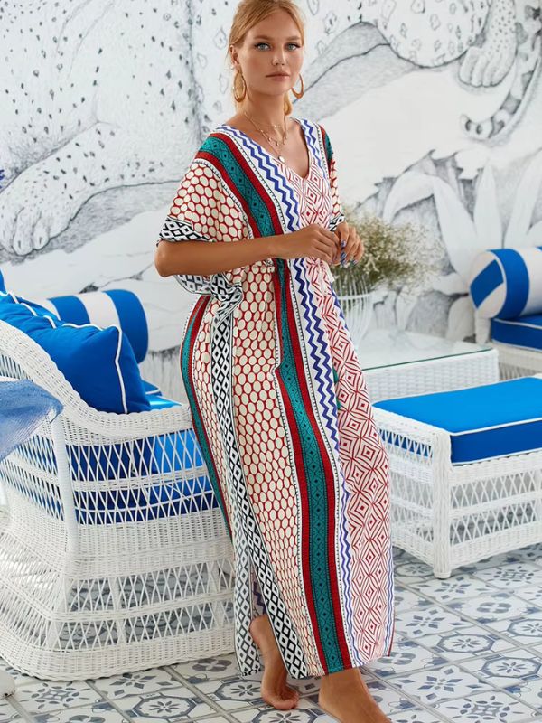 Une femme présente une djellaba colorée aux motifs géométriques, posant de profil dans un intérieur blanc et bleu