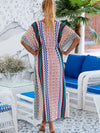 Une femme porte une djellaba longue aux motifs géométriques colorés, vue de dos dans un décor méditerranéen