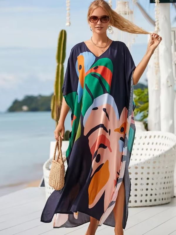 Une femme blonde en djellaba fluide et colorée se tient face à la mer, tenant ses cheveux d’une main