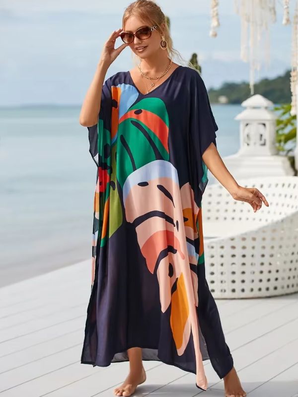 Une femme en djellaba fluide à motifs abstraits profite du bord de mer, tenant une main sur ses lunettes de soleil