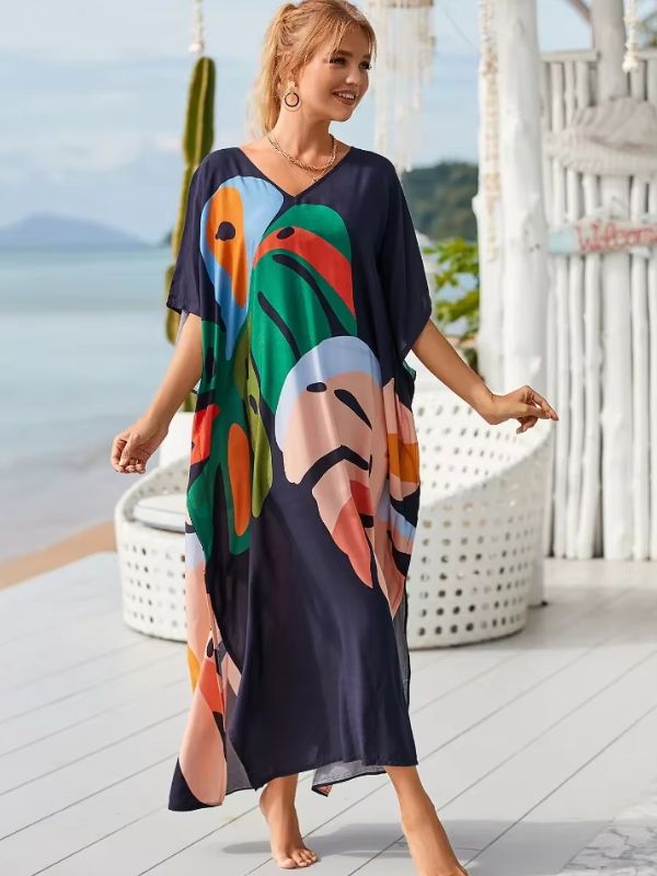 Une femme vêtue d’une djellaba à imprimés de grandes feuilles vertes et orangées marche pieds nus au bord de la mer