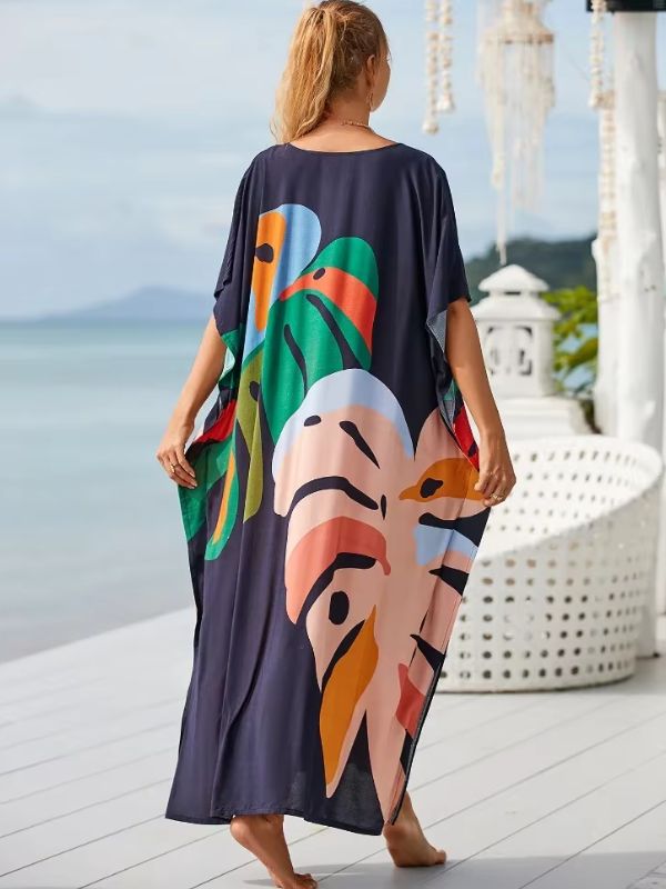 Une femme porte une djellaba fluide aux motifs tropicaux colorés sur une terrasse en bois face à la mer