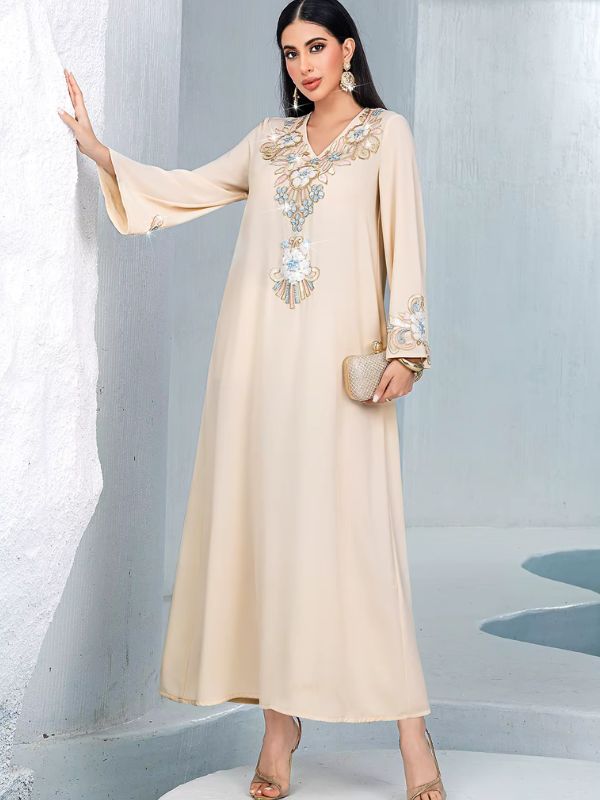 Djellaba marocaine beige brodée de fleurs, vue de face en pied, col en V et manches évasées, mannequin adossée à un mur blanc