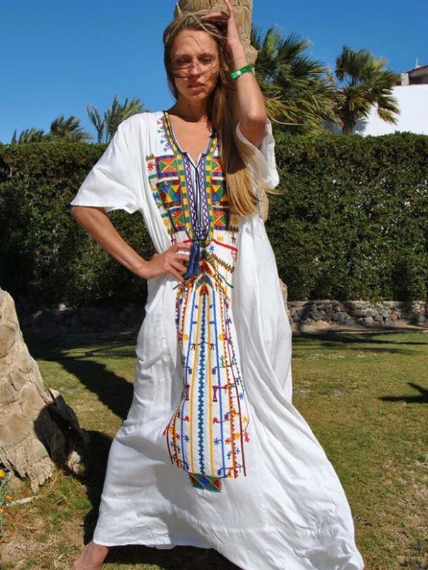 Femme posant en extérieur avec une djellaba blanche à broderies amazighes, une main sur la hanche et l’autre dans ses cheveux