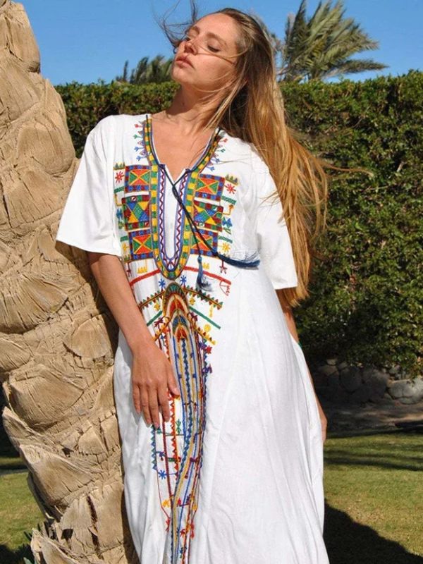 Femme posant en extérieur avec une djellaba blanche à broderies amazighes, une main sur la hanche et l’autre dans ses cheveux