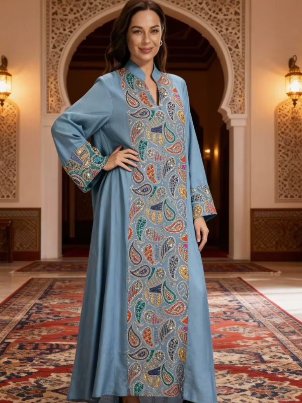 Djellaba marocaine bleu gris, vue de face en pied, col montant à ouverture en V et large bande centrale de motifs cachemire pailletés multicolores, main sur la hanche