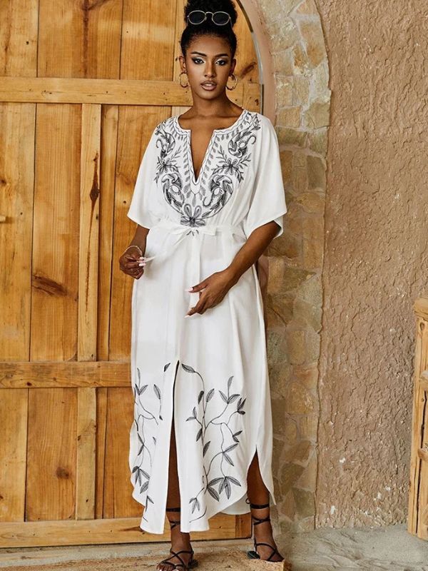 Portrait d’une femme élégante en djellaba blanche ceinturée avec broderies noires, devant une porte en bois