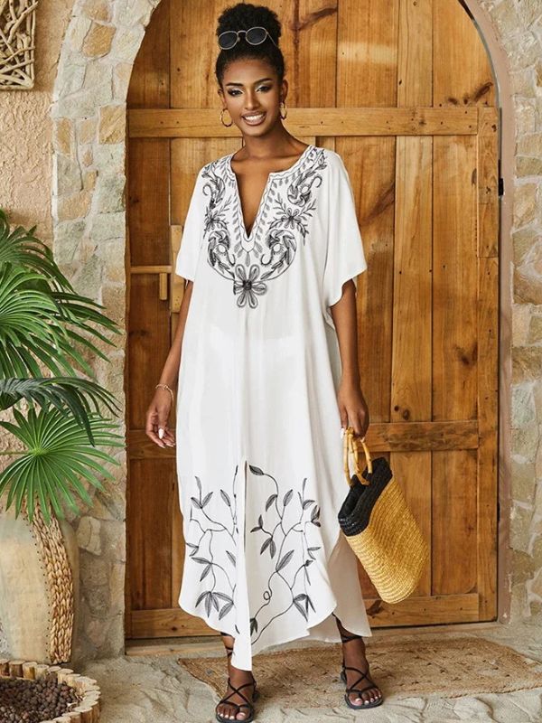 Femme souriante en djellaba marocaine blanche brodée, tenant un sac en osier devant une porte en bois